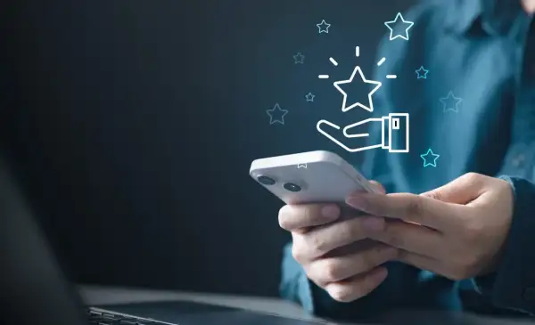 Dłoń trzymająca smartfon z ikoną gwiazdki i dłoni, symbolizującą ocenę.