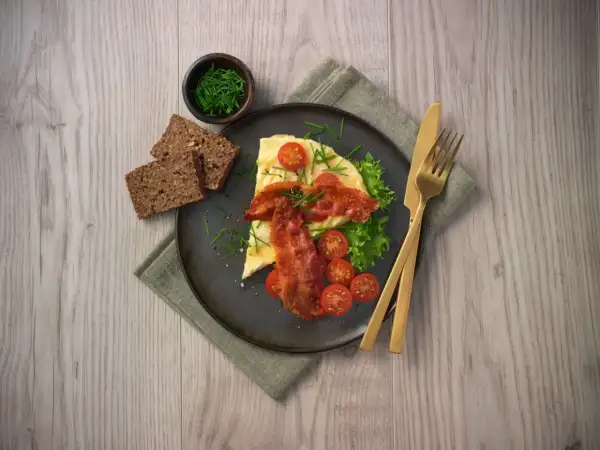 En härlig omelett i ugn med knaperstekt bacon, färska tomater, sallad och grovt bröd. Serveras med gräslök.