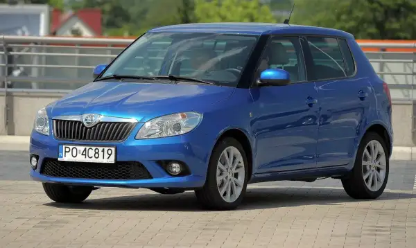 Niebieska Skoda Fabia 2, z nowymi żarówkami w reflektorach, parkuje na placu.