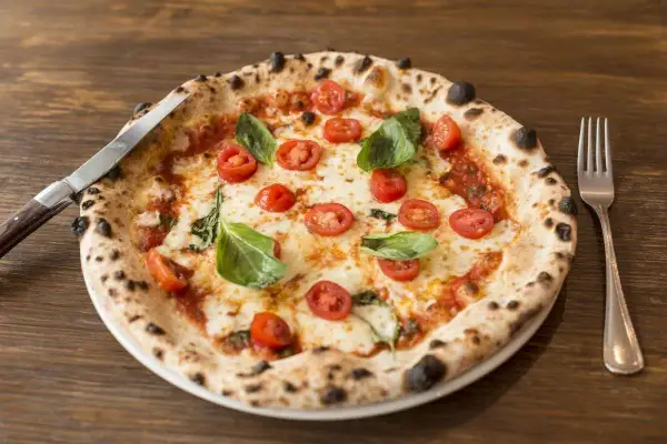 Pizza con lievito madre, pomodorini freschi, mozzarella filante e basilico profumato. Un capolavoro da gustare con coltello e forchetta.
