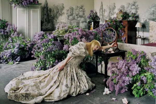 Una mujer rubia con un vestido estampado yace rodeada de lilas, una escena onírica capturada por Tim Walker.