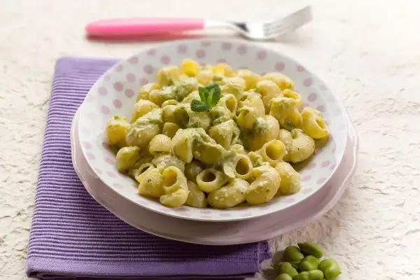 Un piatto di pasta con le fave fresche, condita con una crema verde e guarnita con menta.