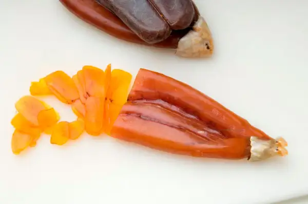 Bottarga en español: huevas de pescado curadas, una entera oscura y otra naranja cortada en láminas finas.