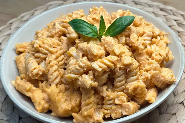 Fusilli conditi con una cremosa salsa al pesto e pomodorini, guarniti con foglie di basilico fresco.