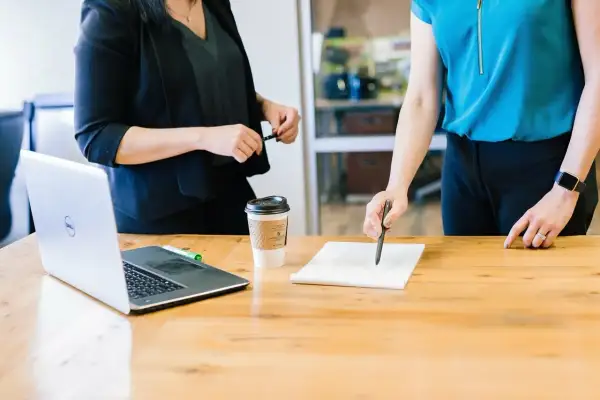 Dwie kobiety omawiają umowę ramową przy biurku z laptopem i kawą.