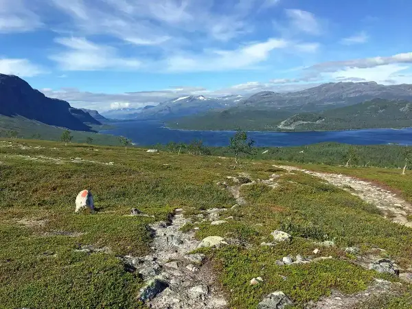 Vacker vy över en sjö och berg, med en stenröse markerad med rött. En vandringsled leder mot horisonten, kanske på väg mellan Kvikkjokk och Saltoluokta.