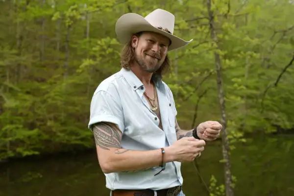 Brian Kelley, in a cowboy hat and light blue shirt, smiles while holding fishing line, perhaps inspired by his songs.