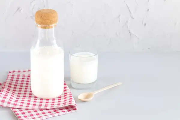 Bouteille de lait et verre sur une serviette à carreaux. Le lait battu, c'est quoi ? C'est ce lait frais et crémeux.