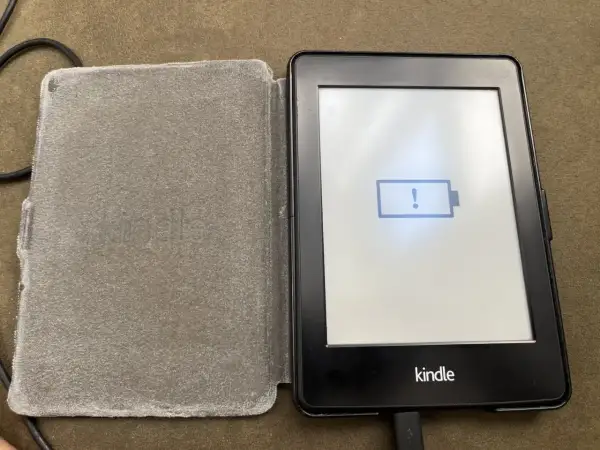 Un Kindle avec une batterie faible, prêt à être éteint. L'icône de batterie vide et le point d'exclamation indiquent qu'il est temps de le charger.