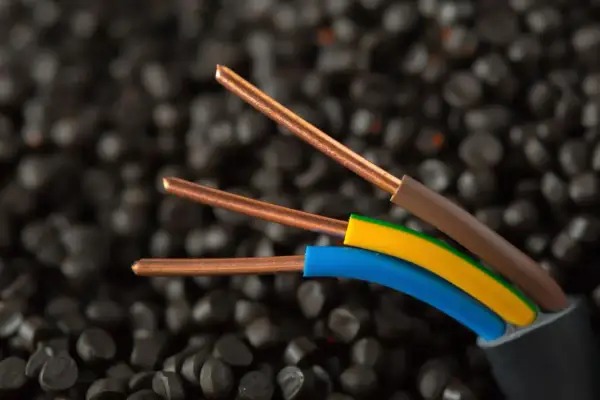 Przewody elektryczne z miedzianymi żyłami i kolorowymi izolacjami (brązowa, żółto-zielona, niebieska) na tle granulatów. IP20 co oznacza? Ochronę przed ciałami stałymi większymi niż 12,5 mm.