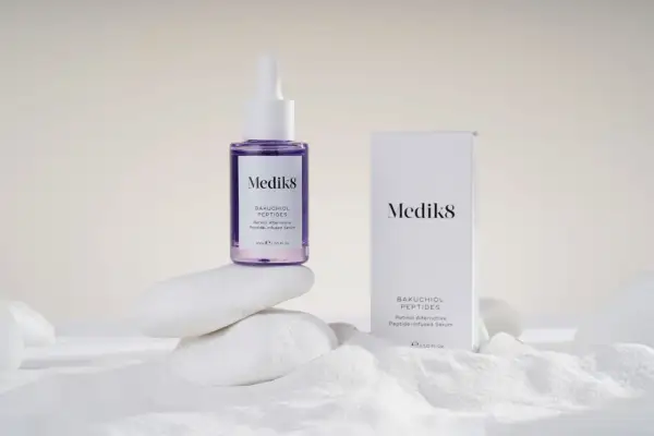 Serum Medik8 z bakuchiolem, roślinnym retinolem, na białych kamieniach i piasku.