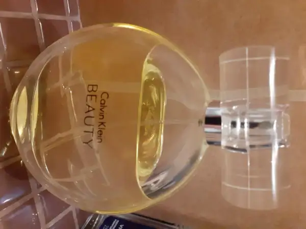 Flakon perfum Calvin Klein Beauty 100 ml, o bursztynowym kolorze, stoi na brązowym tle.