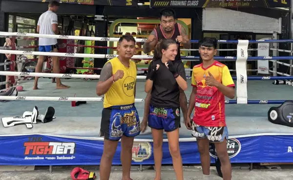 Fyra personer poserar i en ring för c4 thaiboxning. En kvinna i mitten med tränare på var sin sida.