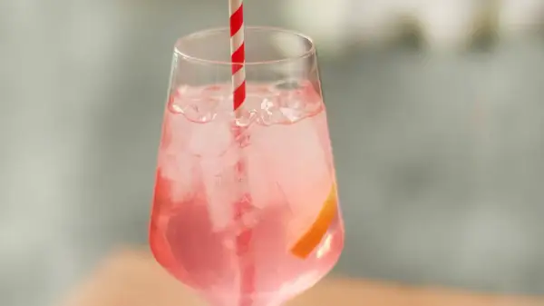 Erfrischender Sarti Spritz mit Eiswürfeln, einer Orangenscheibe und einem rot-weißen Strohhalm.
