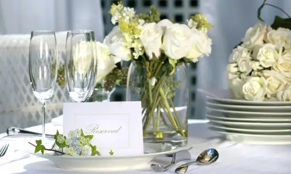 Elegancko nakryty stół z białymi różami, kieliszkami i kartą "Reserved". Idealny na przyjęcie, gdzie wedding planner cena jest kluczowa.
