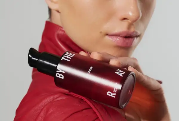 Kobieta w czerwonej ramonesce trzyma buteleczkę z serum. Czy to kwasy PHA jakie to? Delikatne dla skóry, dla blasku.