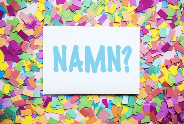 En vit skylt med texten "NAMN?" i ljusblått, omgiven av färgglatt konfetti. Kanske ett unisex namn ska väljas?