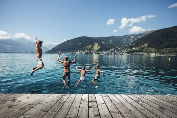 Familj hoppar i vattnet en solig zell am see sommar. Berg och stad i bakgrunden.