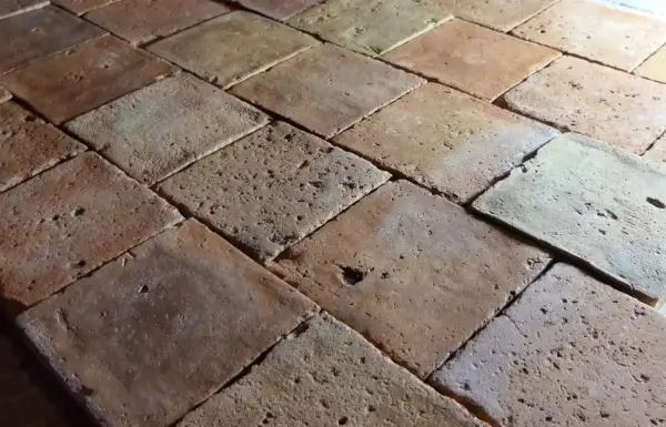 Carrelage en terre cuite, aspect brut et texturé. Chaque carreau présente des variations de couleur et de petites imperfections, témoignant d'un traitement artisanal.