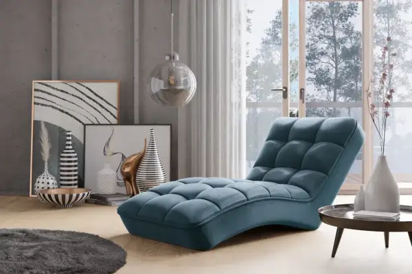 En lyxig, blå schäslong fåtölj med quiltad design står i ett modernt vardagsrum med konst och en stor fönsterdörr.