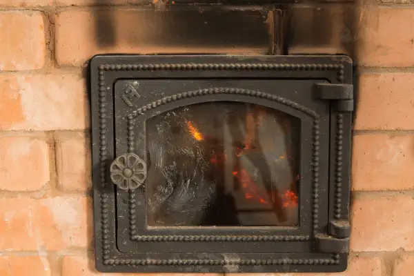 Porta del camino in ghisa annerita dal fumo, con fiamme visibili all'interno. Utile per capire come pulire il marmo del camino annerito.