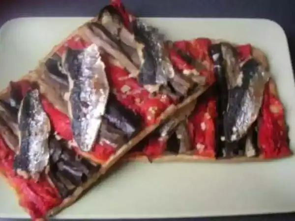 Deux tartes rectangulaires de coca catalane garnies de poivrons rouges, d'aubergines et de sardines, sur une assiette verte.