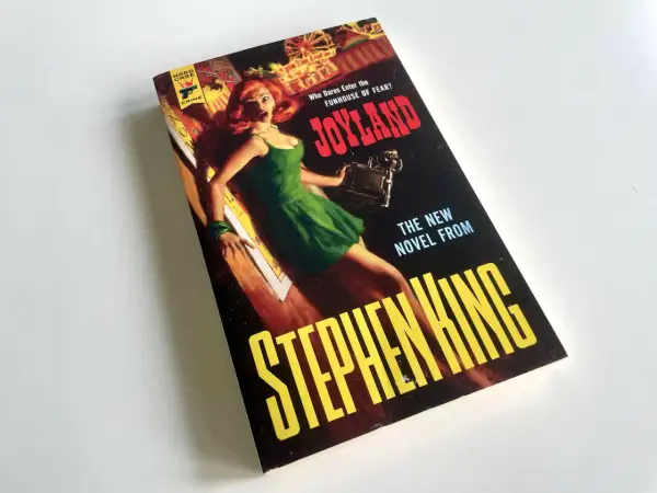Bokomslaget till Stephen Kings "Joyland" med en skräckslagen kvinna i en grön klänning. En av många filmer med Stephen King som väntar på att bli sedd.