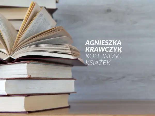 Agnieszka Krawczyk prezentuje nowości w kolejności książek. Stos otwartych i zamkniętych woluminów na tle drewnianej ściany.