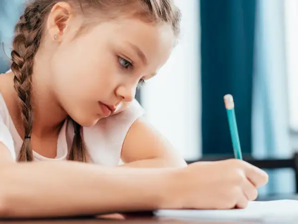 Bambina concentrata scrive con matita. Potrebbe essere una di quei bambini plusdotati 2 anni che già imparano a scrivere.