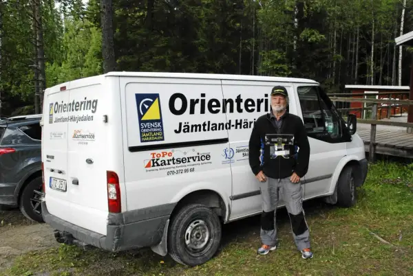 Torgny Pettersson står bredvid en vit skåpbil med texten "Orientering Jämtland-Härjedalen". Han håller i en utrustning för orientering.