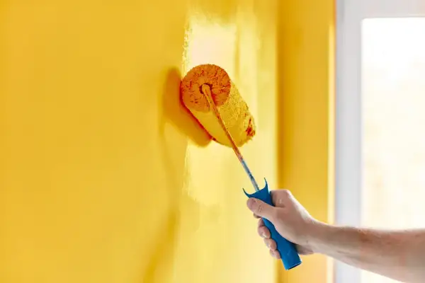 Mano che dipinge un muro di giallo brillante con un rullo. La vernice ha un bellissimo colore opaco che copre uniformemente la superficie.