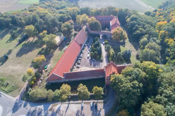 Zamek Bierzgłowski z lotu ptaka, otoczony jesiennym lasem. Widać czerwone dachy, dziedziniec z samochodami i otaczające tereny zielone.