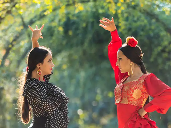 Dos bailarinas de un grupo flamenco famoso, con trajes vibrantes, ejecutan pasos elegantes bajo la luz del sol.