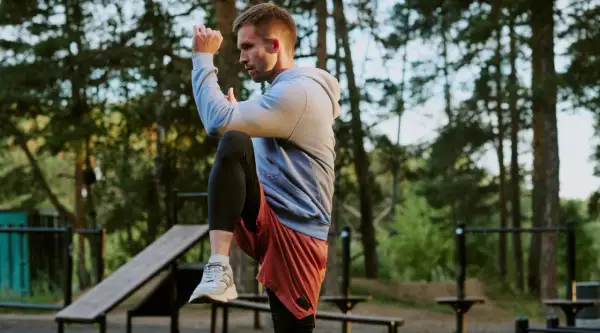 Mann im Freien beim **hit training**, hebt ein Knie, konzentriert sich auf seine Bewegung.