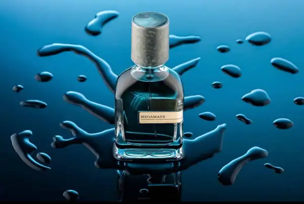 Szklana butelka perfum Megamare otoczona kroplami wody na granatowym tle.