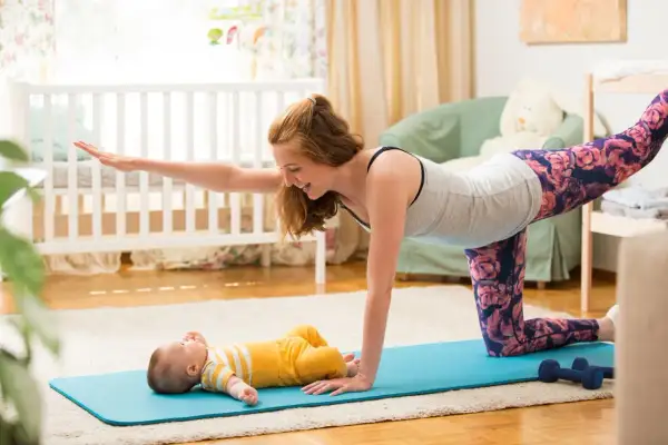 Mama wykonuje ćwiczenia po porodzie na macie, a jej maluch leży obok.