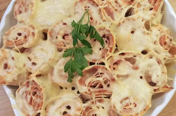 Pyszna tortilla z szynką i serem na ciepło, zapieczona do złotego koloru, udekorowana gałązką natki pietruszki.
