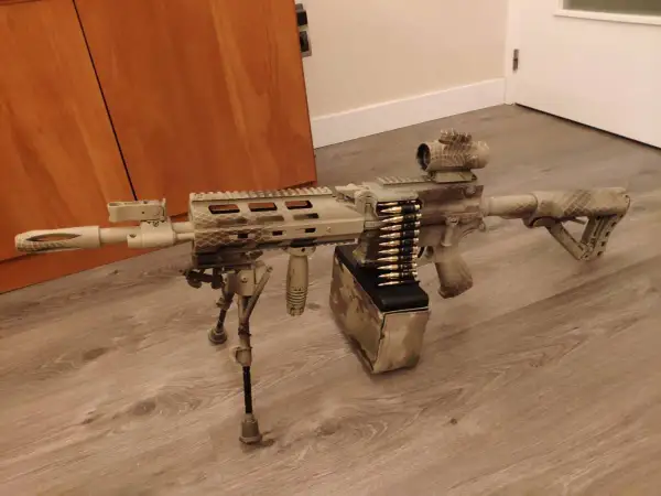 Réplica de airsoft con camuflaje personalizado. El detalle de pintar replica airsoft es impresionante, con un cargador de cinta y mira holográfica.