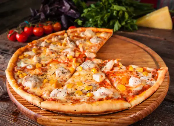 Pyszna pizza z kurczakiem i kukurydzą, podana na drewnianej desce, z pomidorkami koktajlowymi i bazylią w tle.