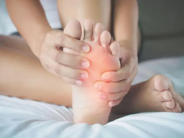 Mani che massaggiano la pianta del piede, evidenziando un'area arrossata che simboleggia il dolore.