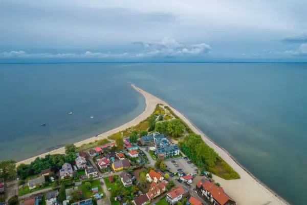 Malownicza miejscowość nad morzem z zabudowaniami i piaszczystą plażą, otoczona spokojnymi wodami.