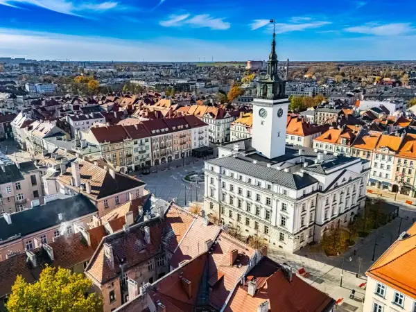 Widok na rynek z ratuszem i wieżą zegarową w najstarszym mieście w Polsce. Dachy kamienic i błękitne niebo.