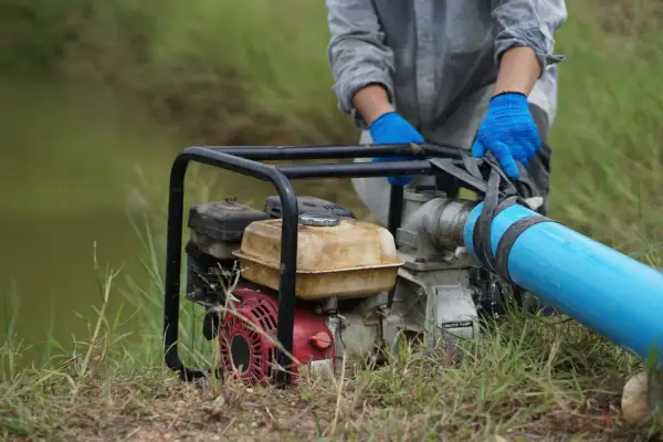 Maintenant, comment démonter une pompe à eau de jardin : une personne en gants bleus manipule le tuyau d'une pompe à eau.
