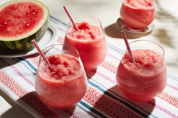 Fryst sallad med vattenmelon i glas med randiga sugrör. En halv vattenmelon ligger bredvid.