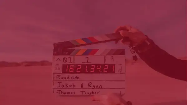 Dłoń trzyma klaps filmowy z zapisanymi informacjami o produkcji.