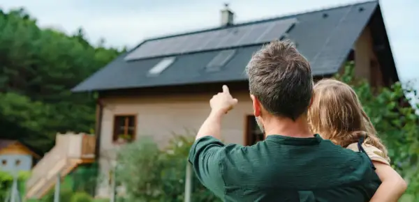 Hombre señala las placas solares virtuales en el tejado de una casa, mientras abraza a una niña.