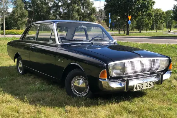 Svart Ford Taunus 1964, en klassisk bil med kromdetaljer, parkerad på en gräsmatta.