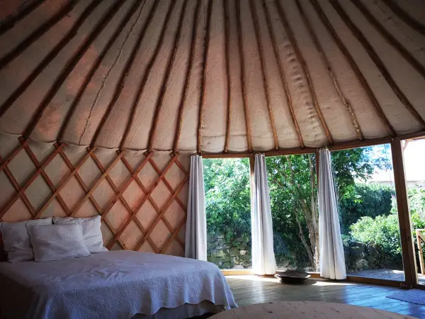 Intérieur d'une yourte gard, lit douillet sous la structure en bois, grandes fenêtres offrant une vue sur la verdure.