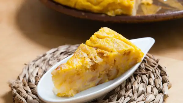 Una porción de tarta de choclo, dorada y apetitosa, servida en un plato blanco sobre una esterilla tejida.