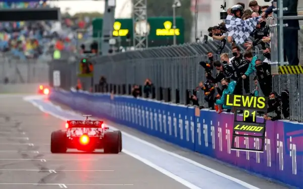 Un coche de Fórmula 1 cruza la meta, con el equipo celebrando la victoria de Lewis Hamilton en el gran premio.